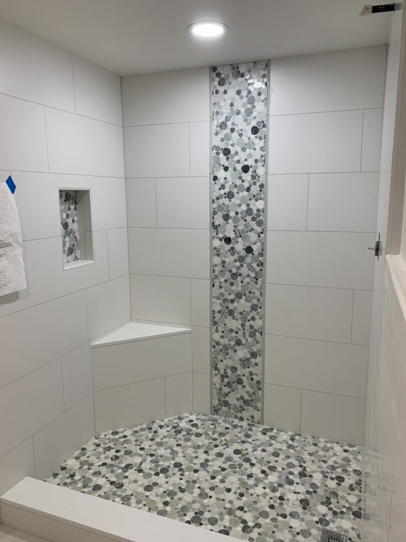 A white and gray tiled shower with a tiled floor.